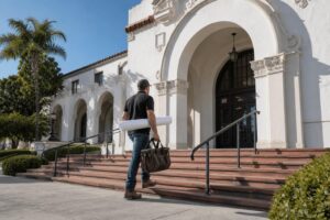 Contractor carrying rolled blueprints at a Spanish Colonial Revival municipal building, preparing a remodeling permit application with the Santa Barbara building department